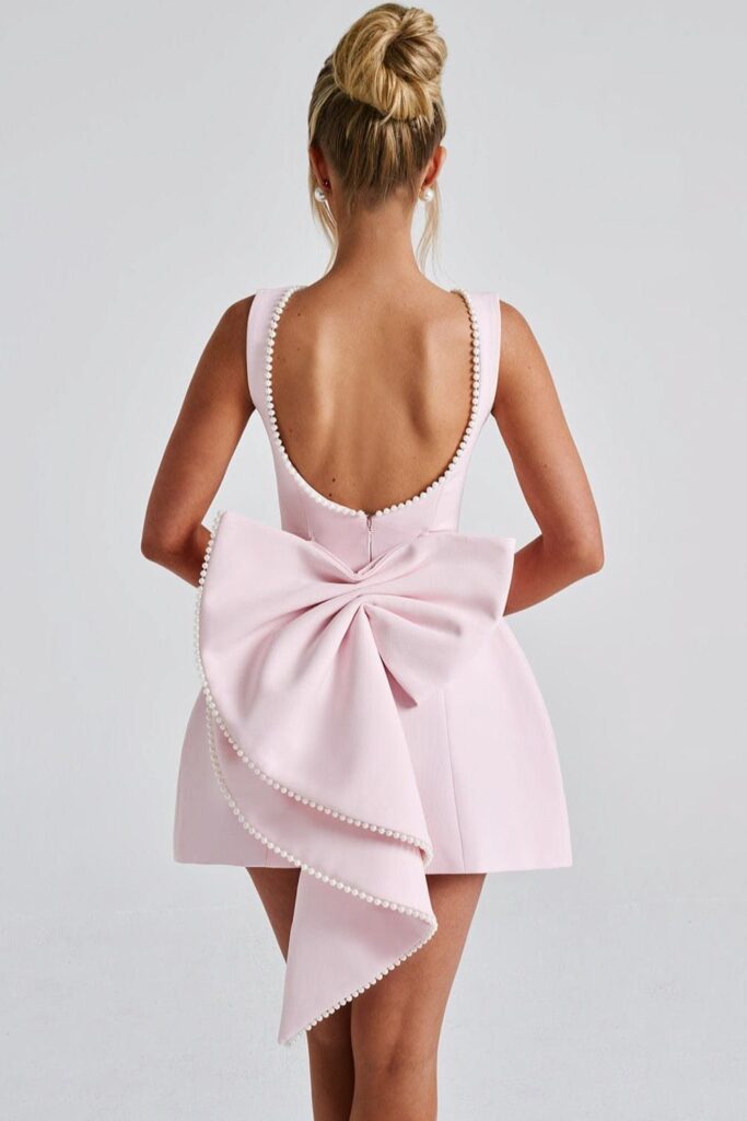 Rear view of a woman wearing a light pink graduation dress with a large bow and pearl trim