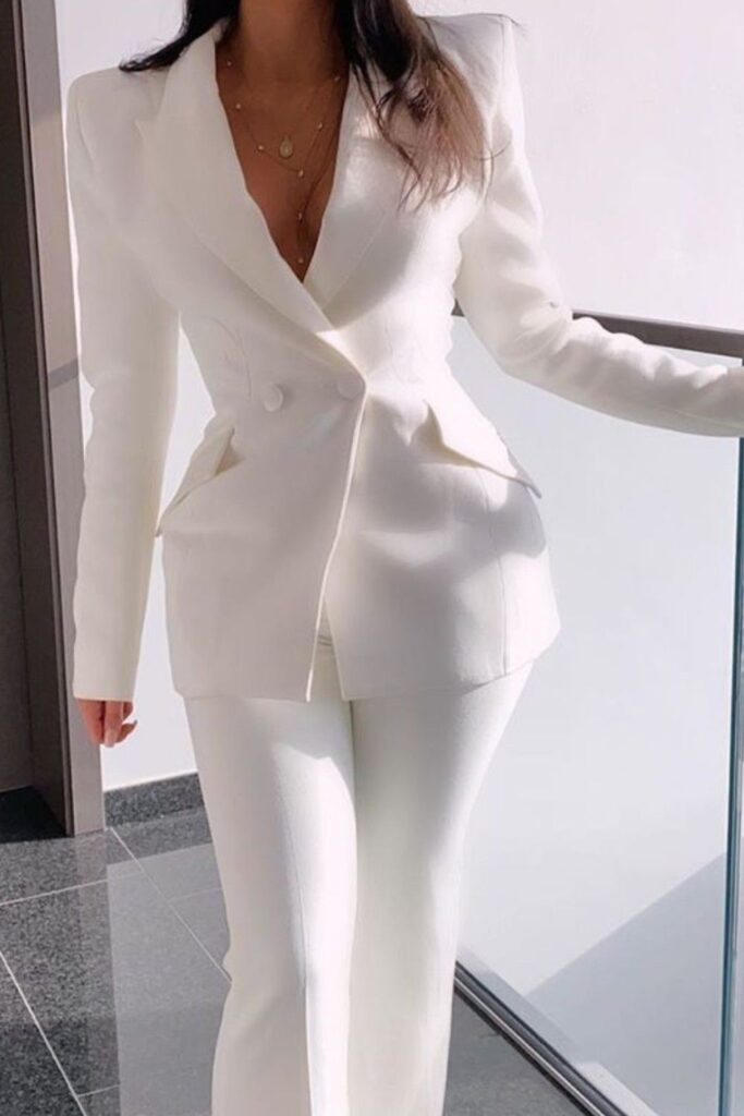 Woman wearing a fitted white pantsuit with a structured double-breasted blazer and matching trousers.