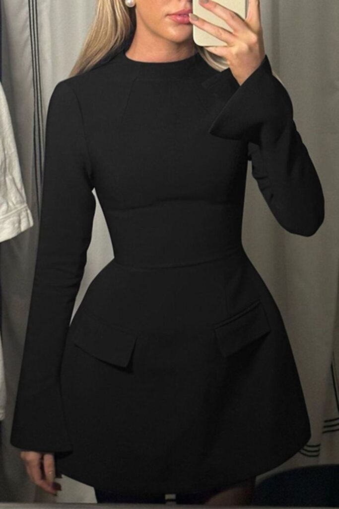Woman taking a mirror selfie wearing a structured black long sleeve mini dress with pocket flap details.